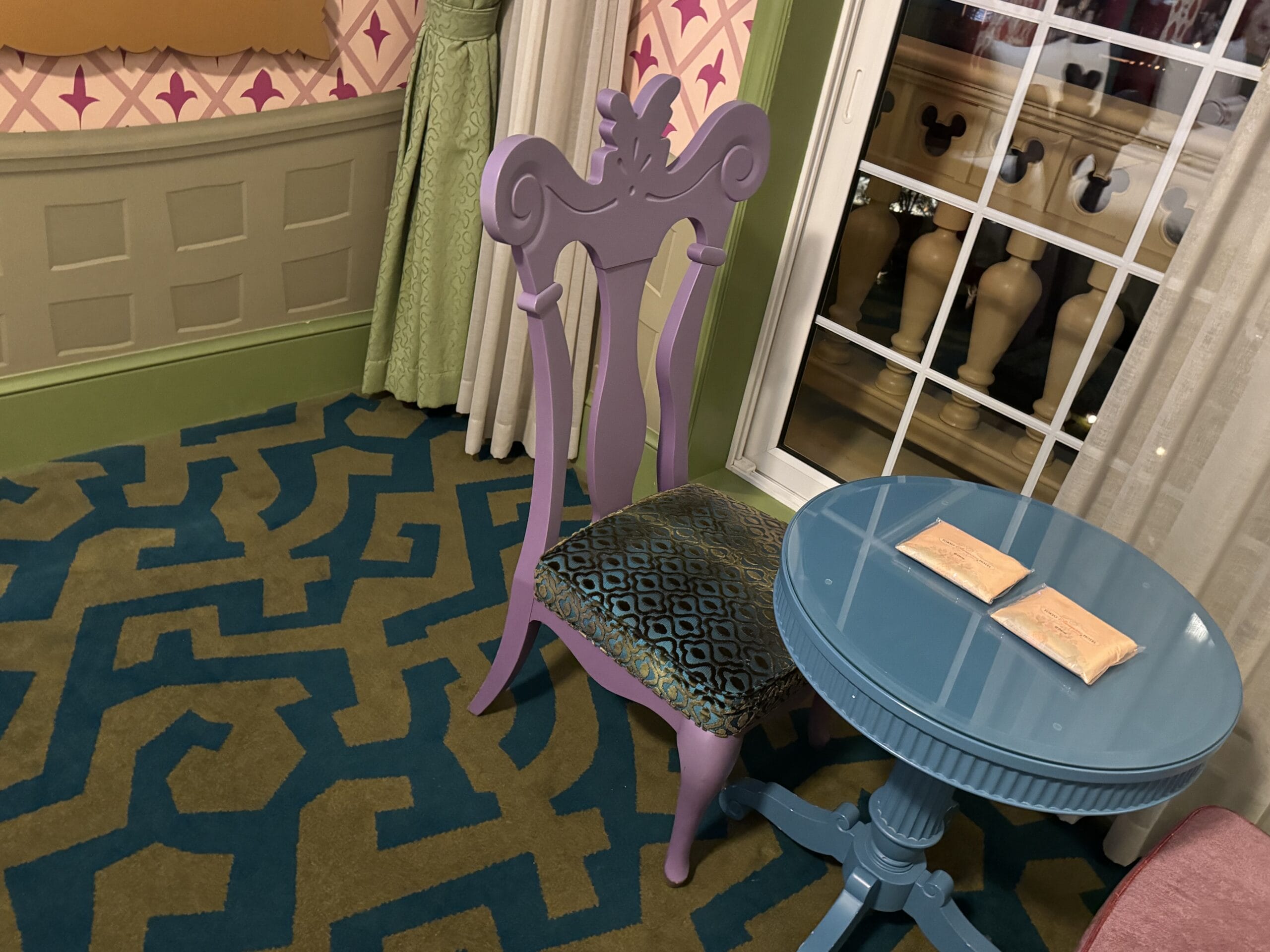 A purple ornate chair and blue table with envelopes in an Alice in Wonderland Hotel Room at Tokyo Disneyland Hotel.