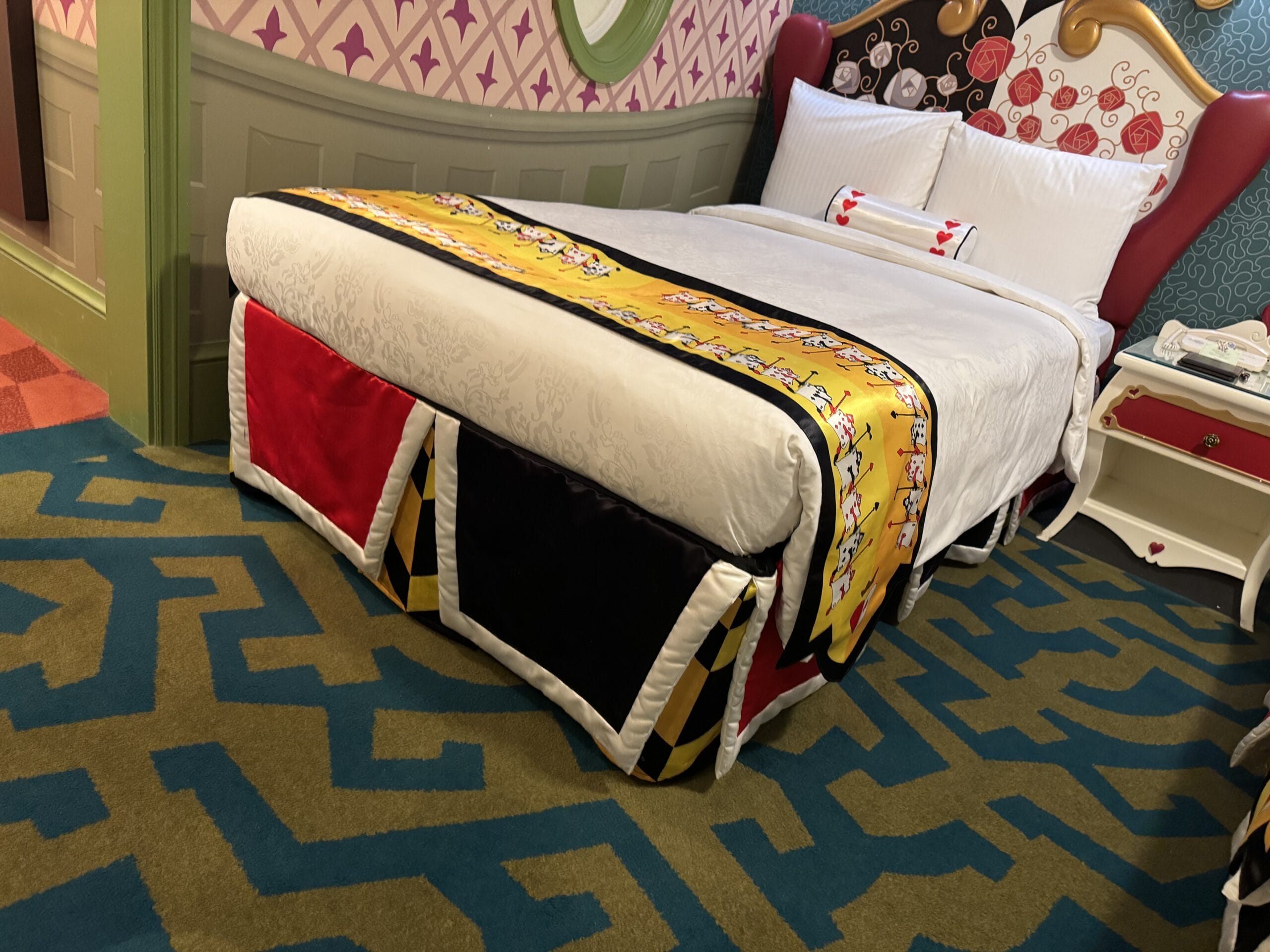 A single bed with a colorful Alice in Wonderland-themed bedspread in a whimsical Tokyo Disneyland Hotel room.