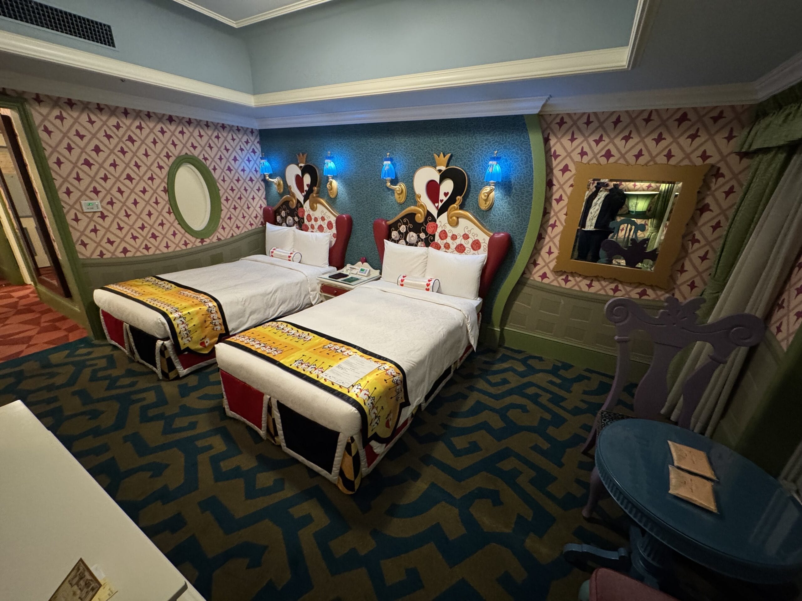 Whimsical Alice in Wonderland hotel room with twin beds, heart headboards, and playful card-inspired decor at Tokyo Disneyland Hotel.