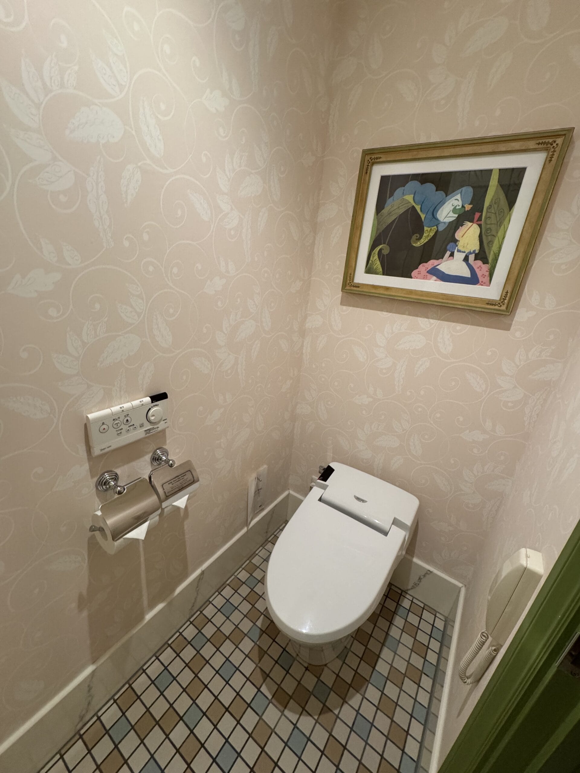 A modern toilet with a bidet, two toilet paper rolls, and Alice in Wonderland decor in a Tokyo Disneyland Hotel room.