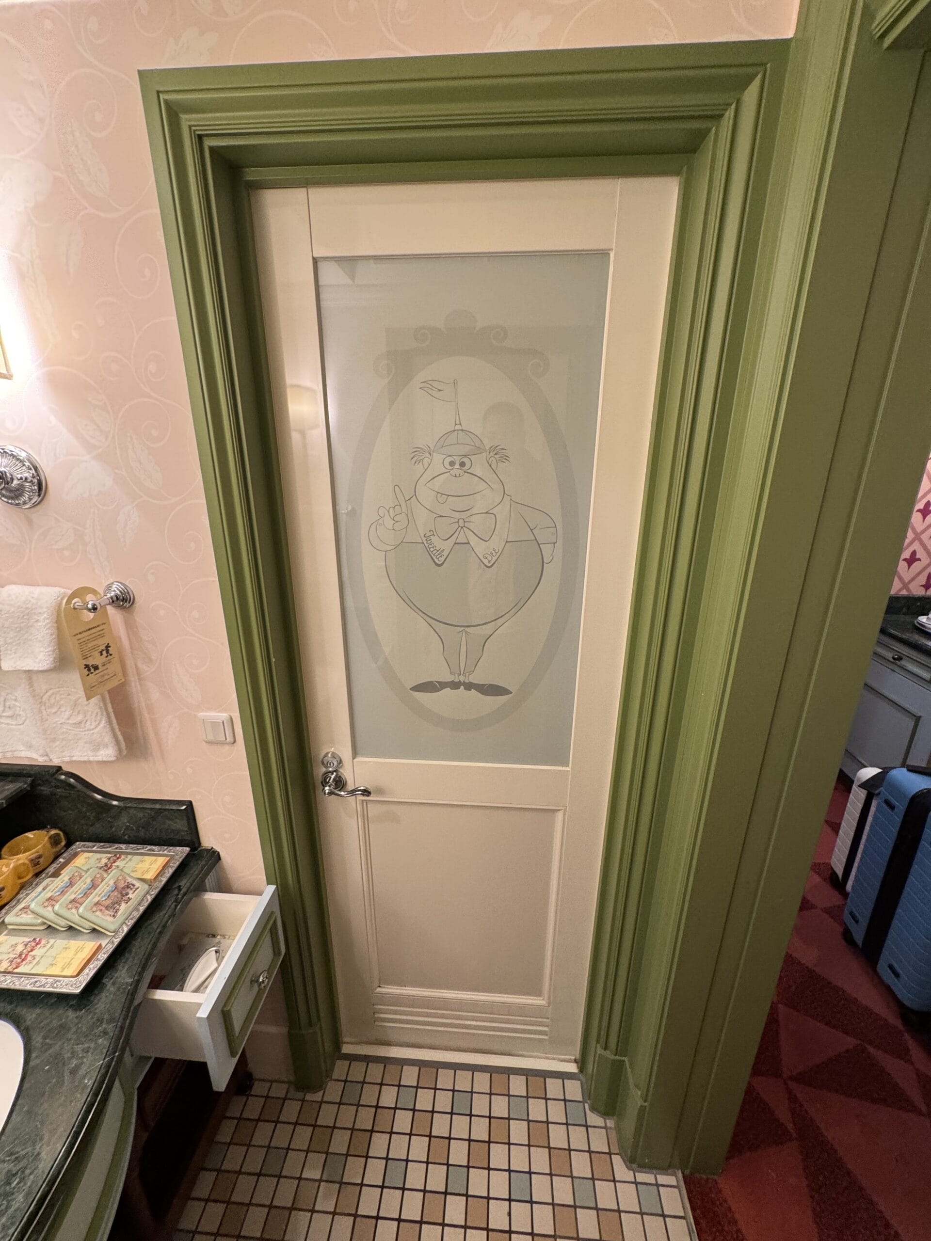 A white door with a cartoon waiter on frosted glass, framed in green, adds whimsy to this Alice in Wonderland hotel bathroom.