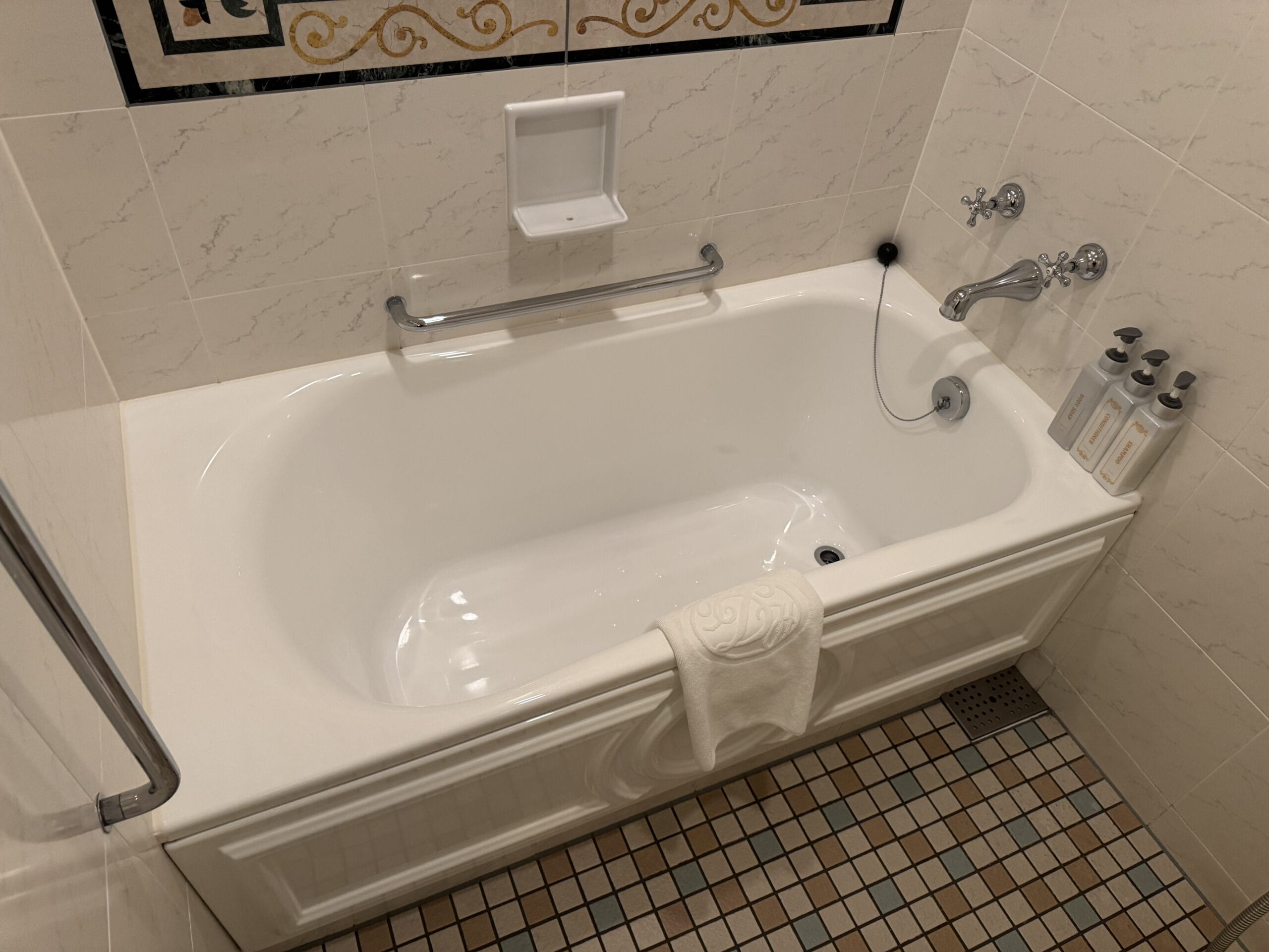 White bathtub with grab bars in an Alice in Wonderland hotel room at Tokyo Disneyland Hotel, tiled floor and wall shower.
