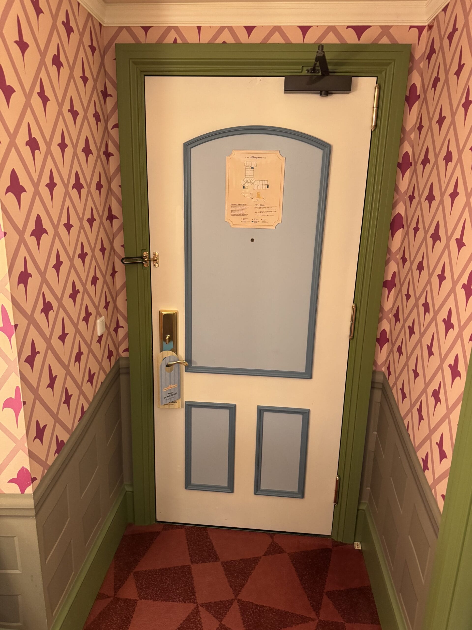 A closed white door with blue panels and green trim, like an Alice in Wonderland hotel room at Tokyo Disneyland Hotel.