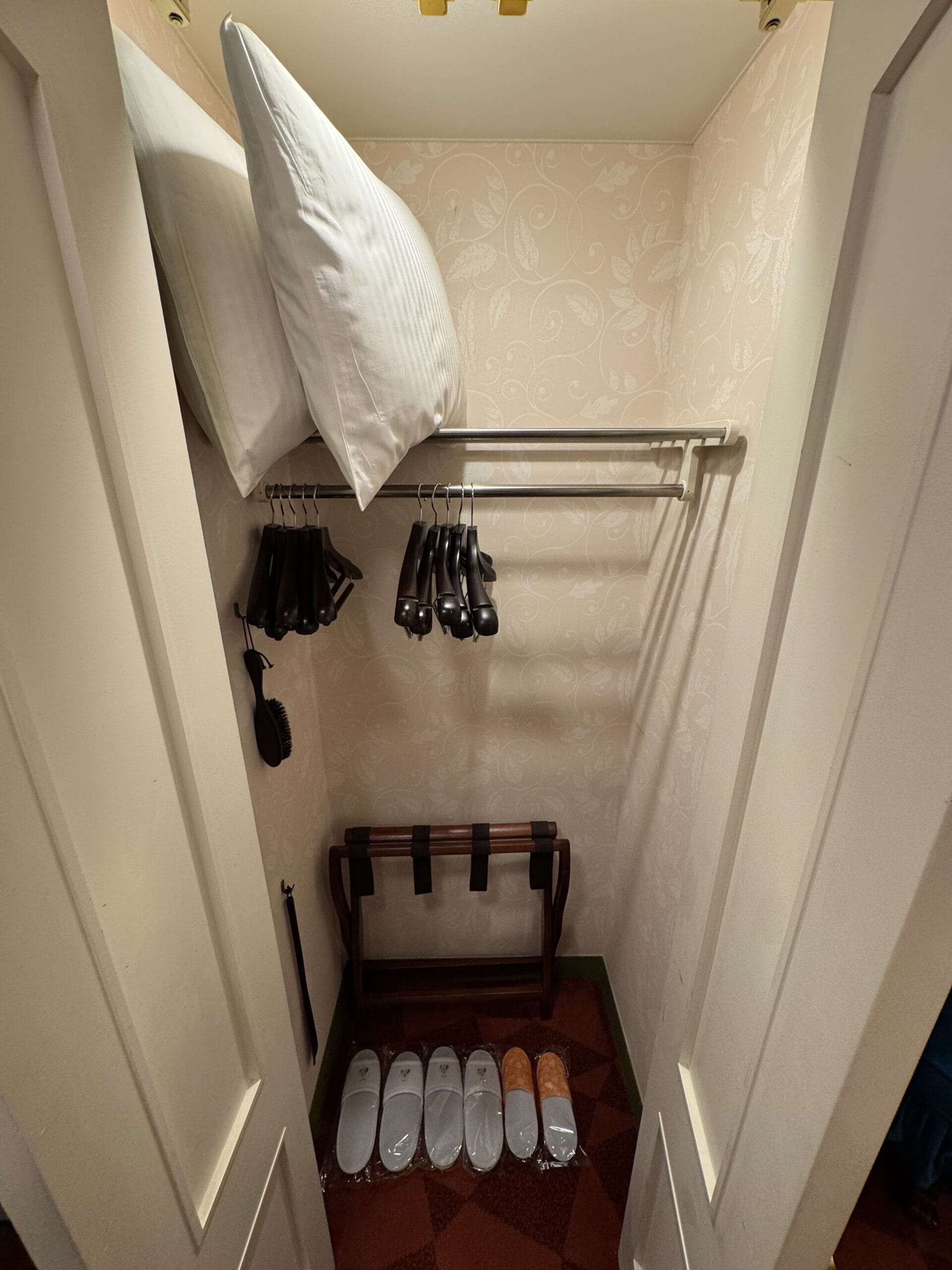 Small closet in the Tokyo Disneyland Hotel with pillows, hangers, a luggage rack, and neatly arranged slippers.