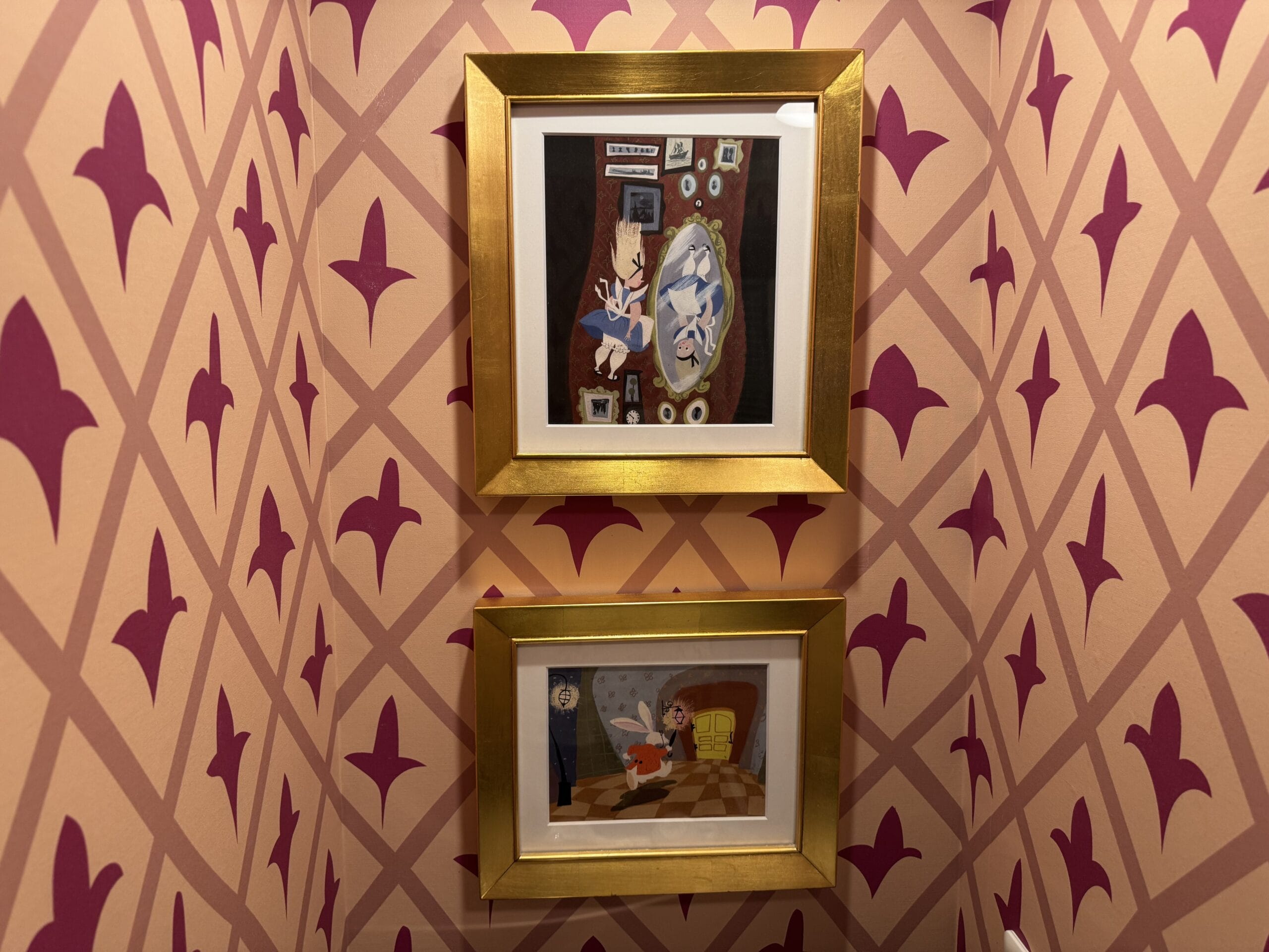 Two framed cartoon prints hang in an Alice in Wonderland Hotel Room with a pink and purple geometric pattern.