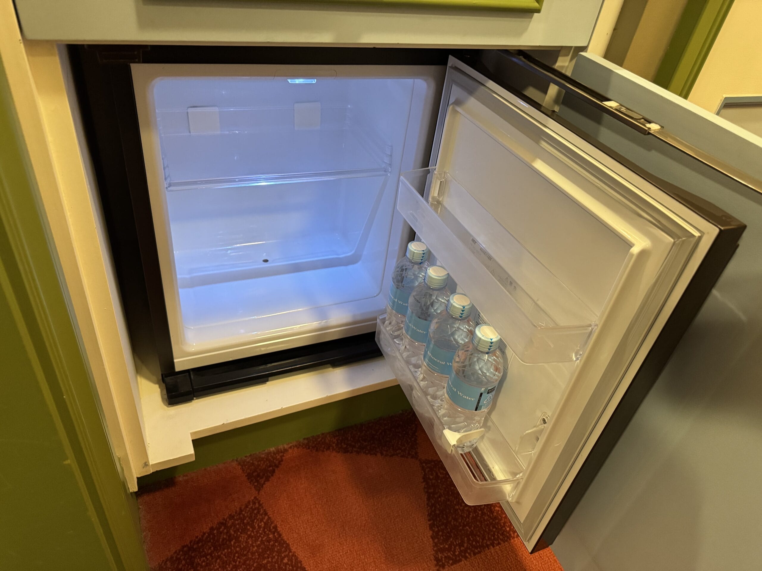 An open mini fridge in a Tokyo Disneyland Hotel room with four bottles of water—perfect for your Alice in Wonderland hotel tour.