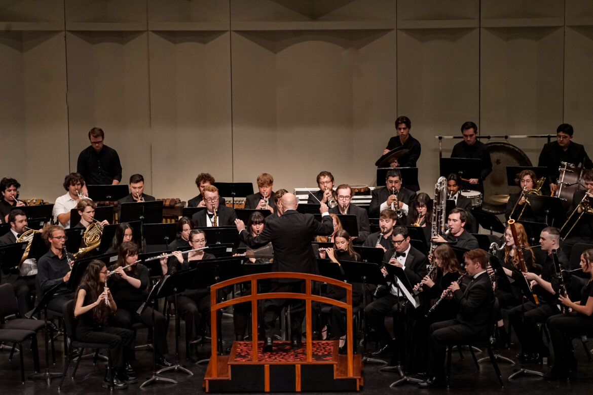 a group of musicians playing various wind instruments onstage with a conductor in front of them.