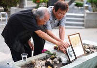 Genshin Maeshiro, 92, left, places a portrait of his older brother Gensho at the Konpaku-no-to Monument in Itoman, Okinawa Prefecture, on Okinawa Memorial Day, June 23, 2025. He commented, 