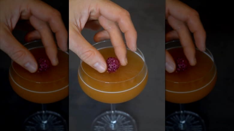 A hand places a garnish on a red akuma cocktail
