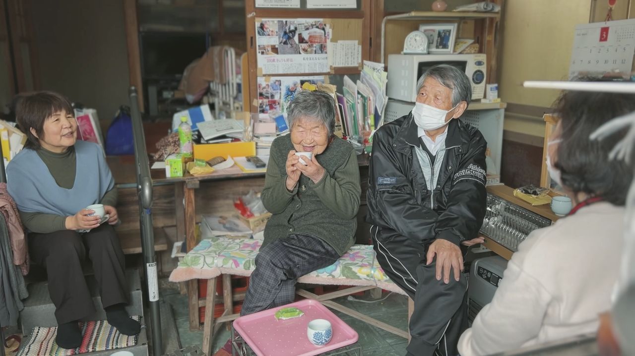 Relatives and neighbors came to welcome Tetsuyo home from the hospital. (© 104-Hitori Production Committee)