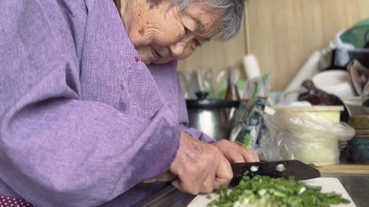 Tetsuyo chops spring onions with a well-worn knife. (© 104-Hitori Production Committee)