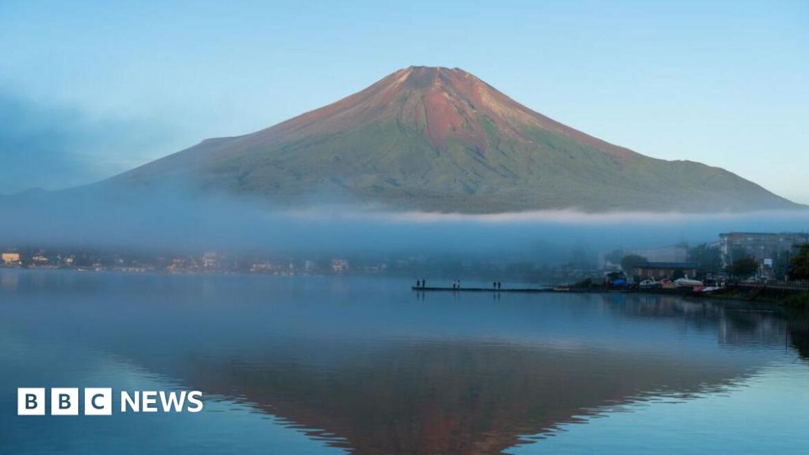 A wide shot of Mount Fuji seen without snow, silhouetted in a blue lake, in September last year