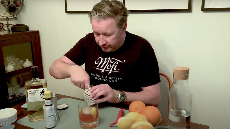 A man sits at a table mixing a Japanese old fashioned cocktail, with the ingredients to make it around him