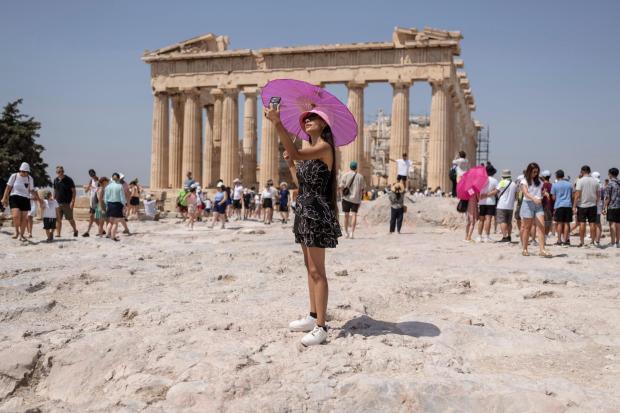 FILE - A woman takes a selfie in front of Parthenon temple atop of the ancient Acropolis hill during a heat wave in Athens, Greece, July 21, 2023. (AP Photo/Petros Giannakouris, File)