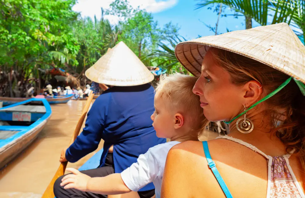 Happy family ride on traditional Vietnamese boat by yellow brown water in canal. Mekong river delta