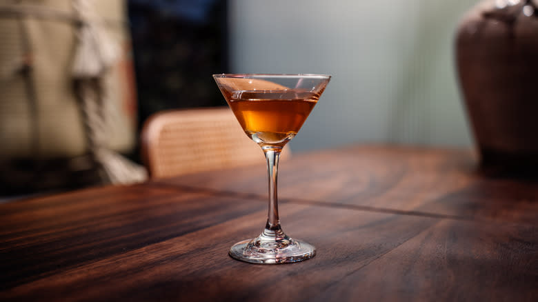 A cocktail in a coupe glass sits on a wooden table
