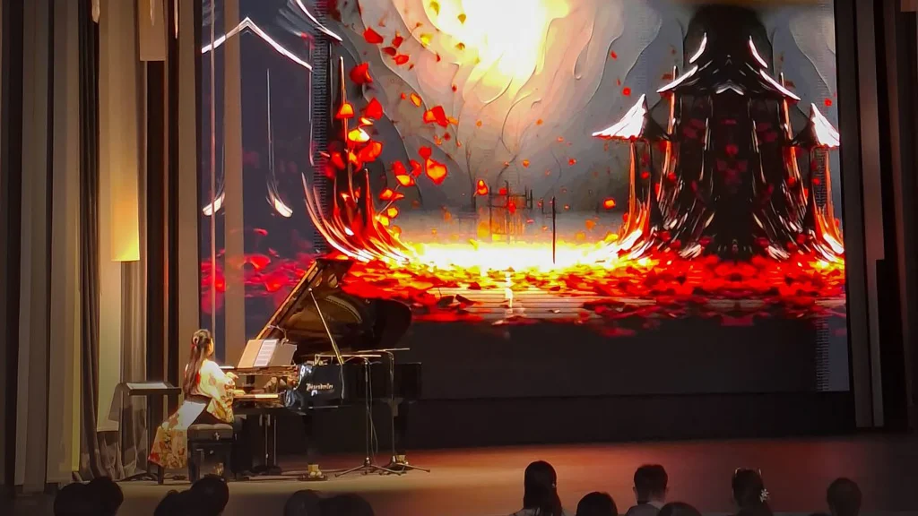 A pianist plays a grand piano mixed up to a computer on stage in front of a giant screen showing abstract images at Expo 2025