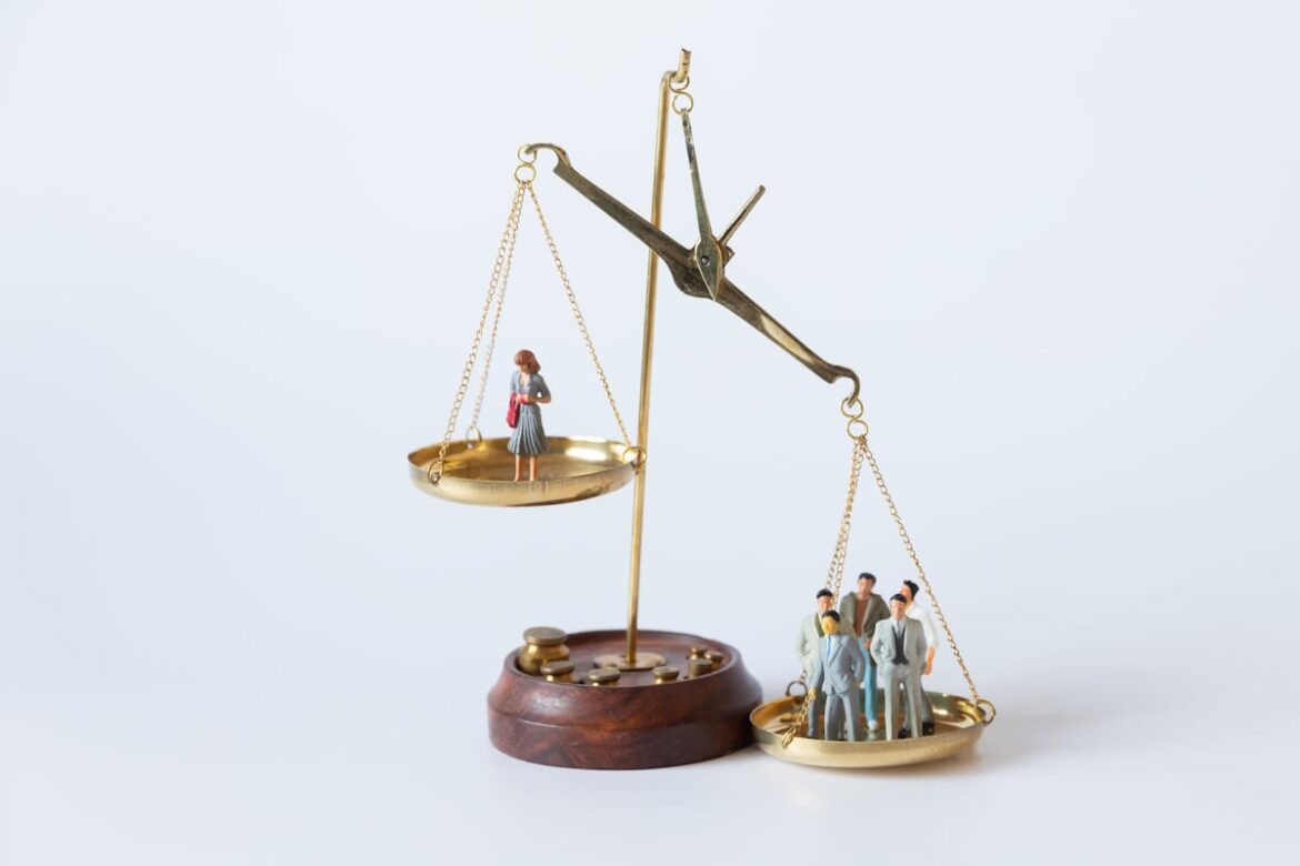 2025 Gender Gap Report Finds Japan Still at Bottom of G7 A set of scales with a single woman on the left being outweighed by a group of men on the right. The people are represented using dolls.