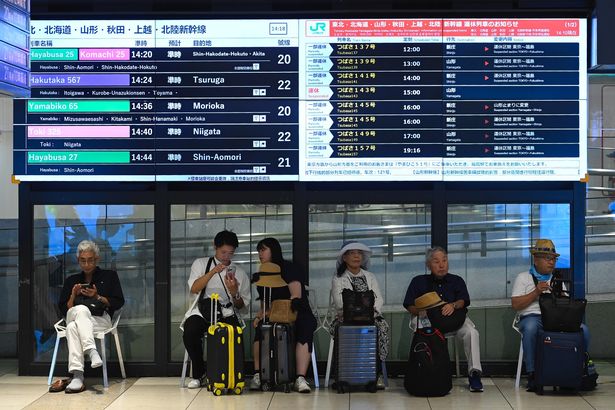 Travelers are waiting in Tokyo Station under a sign announcing the cancellation of some trains following a tsunami alert on July 30, 2025, in Tokyo, Japan