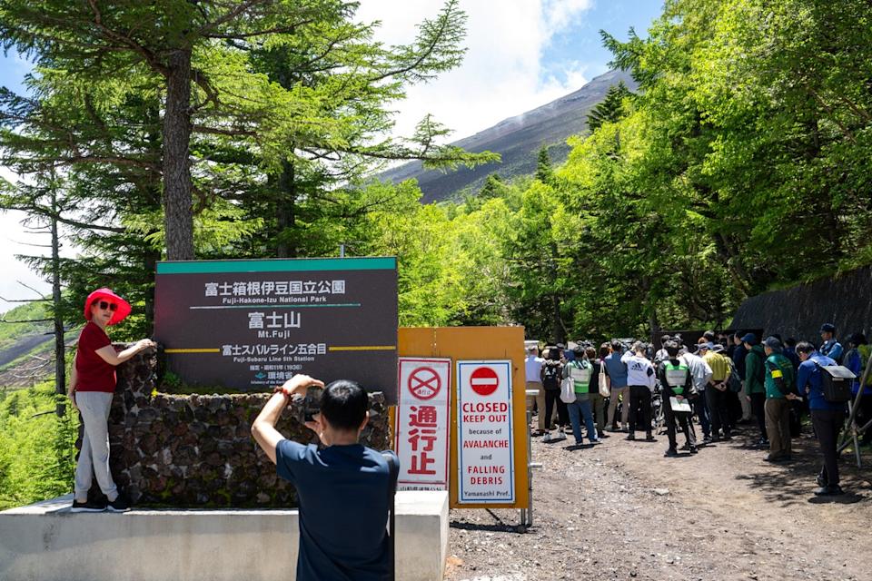 File. A tourist (L) poses in front of the gate of Fuji-Hakone-Izu national park near the Fuji Subaru Line 5th station, which leads to the popular Yoshida trail for hikers climbing Mount Fuji, at Narusawa, Yamanashi prefecture (AFP via Getty Images)
