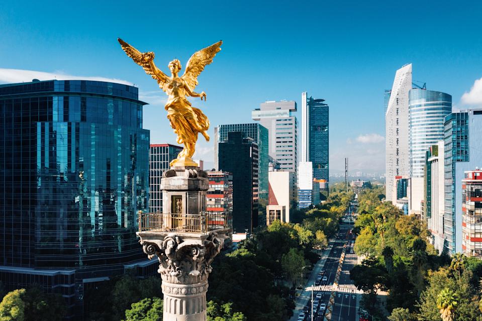 Angel of Independence statue overlooking cityscape with modern skyscrapers in Mexico City, featuring tree-lined avenues and bustling urban environment