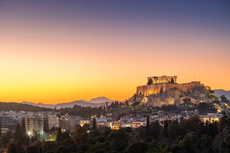 The Acropolis in Athens at sunset, with a view of the cityscape and distant mountains under a clear sky