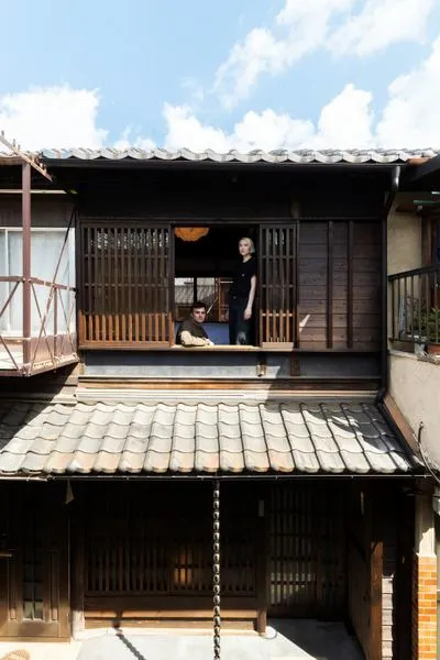 Photographer Dominick Sheldon and set designer Whitney Hellesen look out from the upper level of their <i>machiya</i>, or townhouse, in Kyoto, Japan. The couple renovated the pre-1950s structure as a photography library, gallery, and artist residency. With an eye to restoring traditional elements while injecting a touch of modernity, they added wood slats and <i>yakisugi </i>panels to the previously nondescript upper facade.