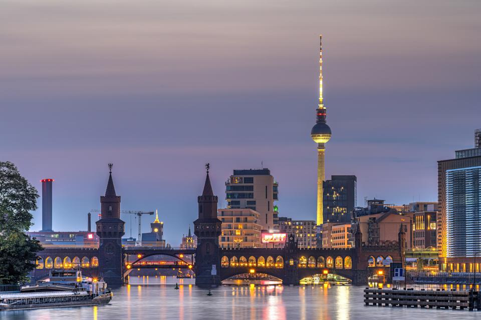 Berlin skyline at dusk, featuring the TV Tower and Oberbaum Bridge reflecting in the Spree River, with modern buildings in the background