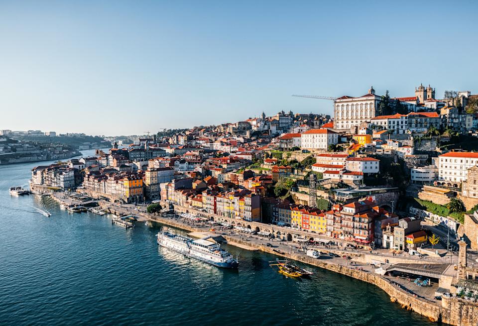 Scenic view of a coastal city with terraced buildings along the waterfront, boats on the river, and hills in the background