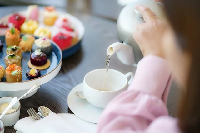 Prasit photo/Getty Images A person pouring tea into a tea cup next to a plate filled with small snacks.