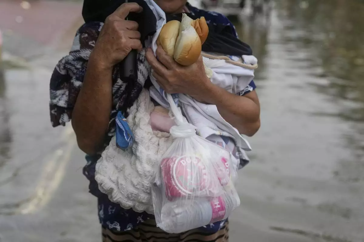 A resident carries items from her flooded home as intense rains continue due to the southwest monsoon at Malabon city, Philippines on Thursday, July 24, 2025. (AP Photo/Aaron Favila)