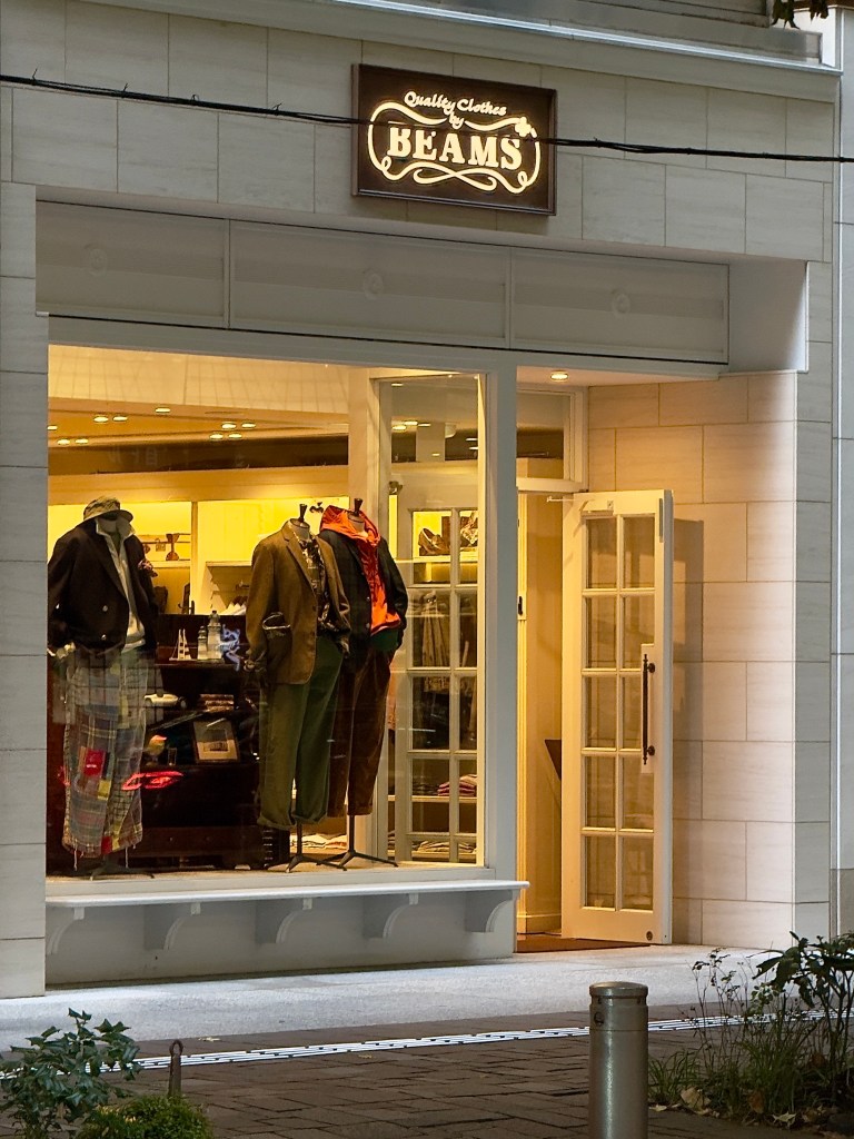 An exterior of Beans + showing clothing in a store window with a door open.