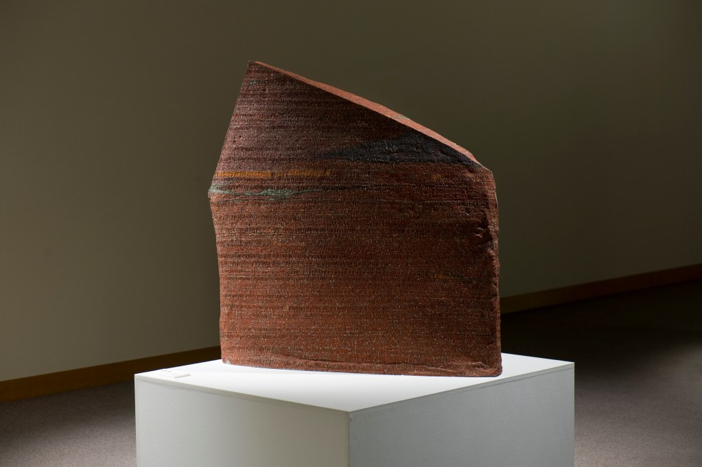 A rust-colored sculpture on a white pedestal.