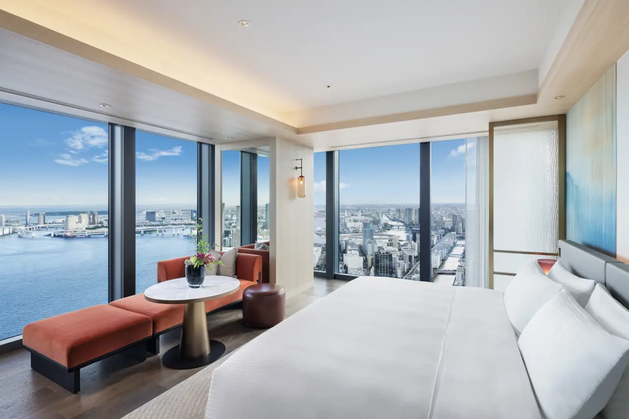 Luxurious Fairmont Tokyo guest room with floor-to-ceiling windows, offering panoramic views of Tokyo Bay and the city skyline, featuring a modern seating area and king-size bed.