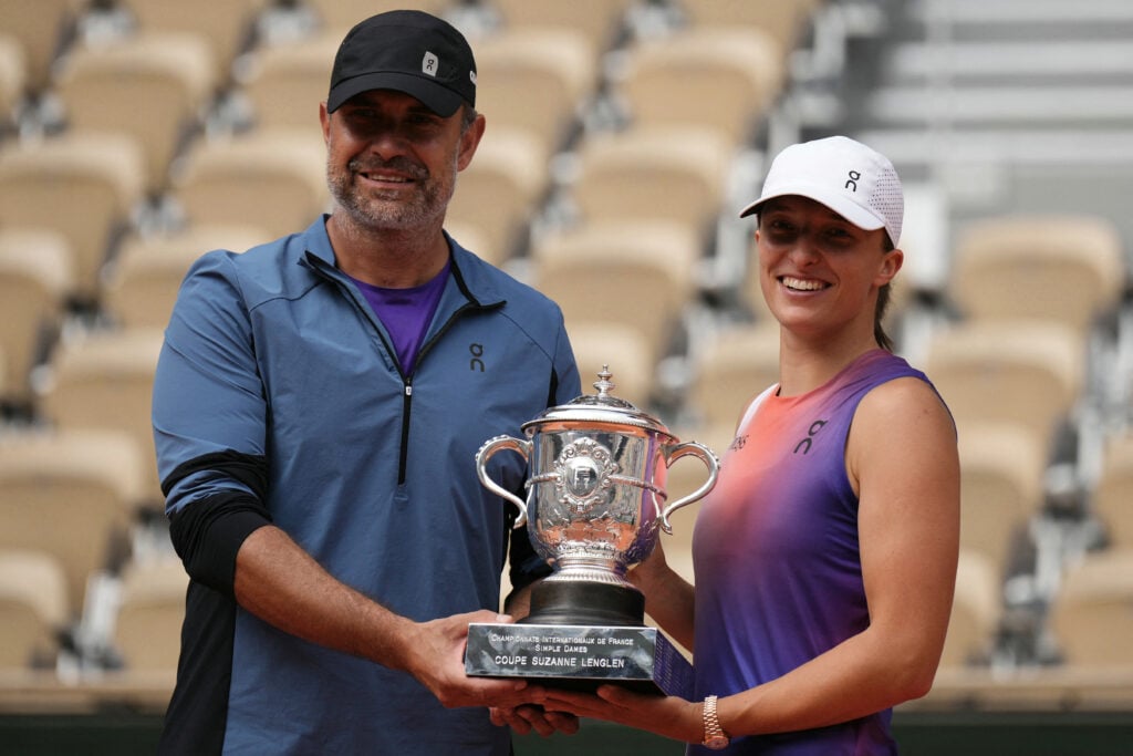 Iga Swiatek poses with her coach Tomasz Wiktorowski with the trophy after winning against Italy's Jasmine Paolini at the end of their women's singles final match on Court Philippe-Chatrier on day fourteen of the French Open tennis tournament at the Roland Garros Complex.