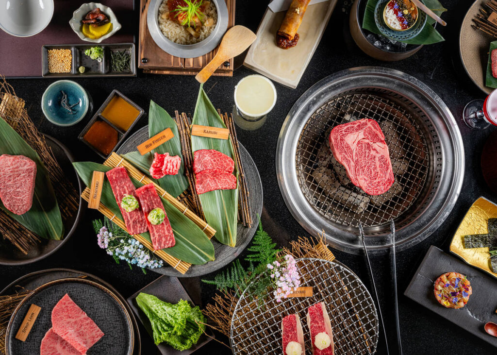 a table overladen with cuts of Wagyu and a steak cooking on a grill in the table itself