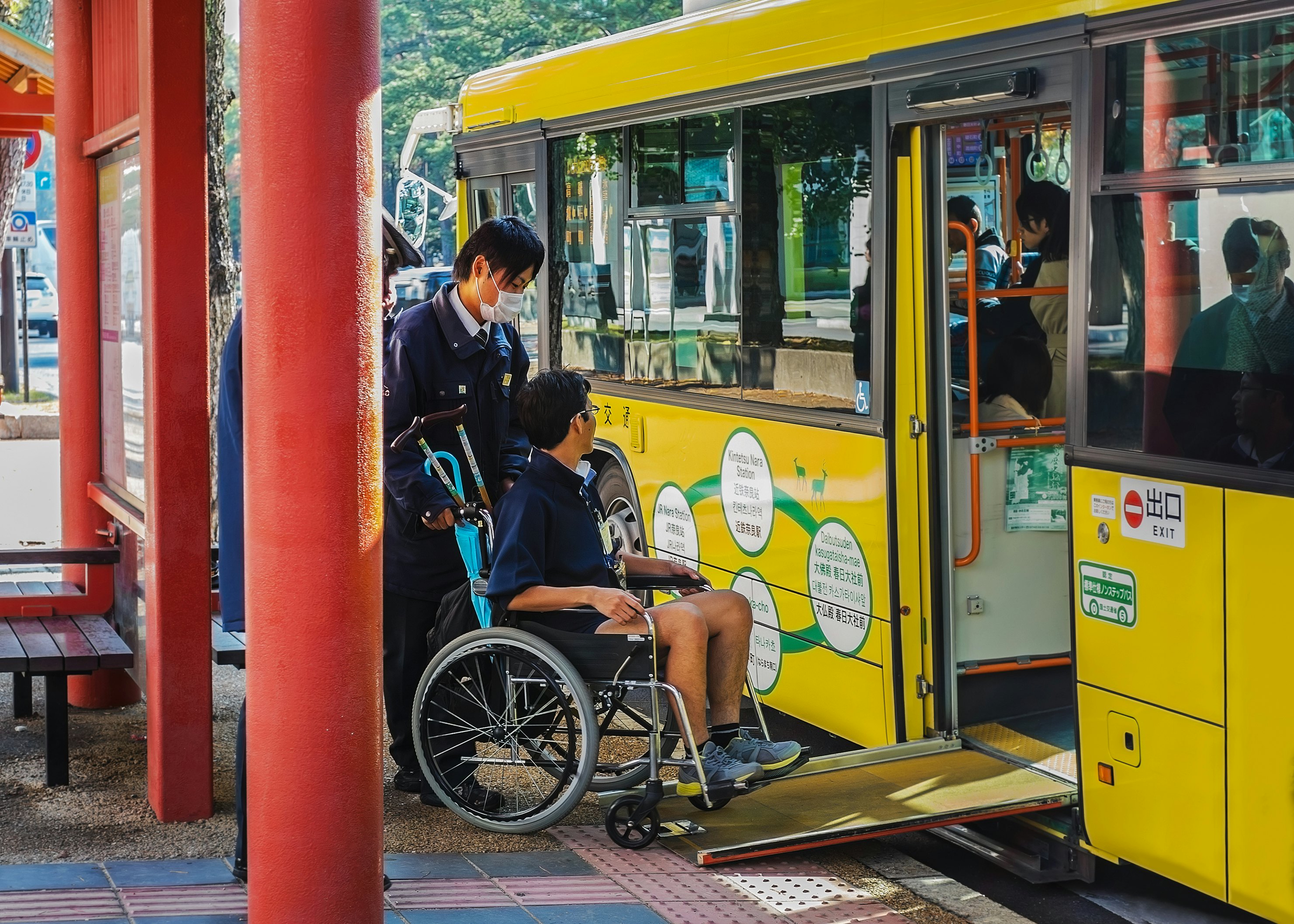 A man in a wheelchair boards a yellow bus via a temporary ramp in Nara, Japan.