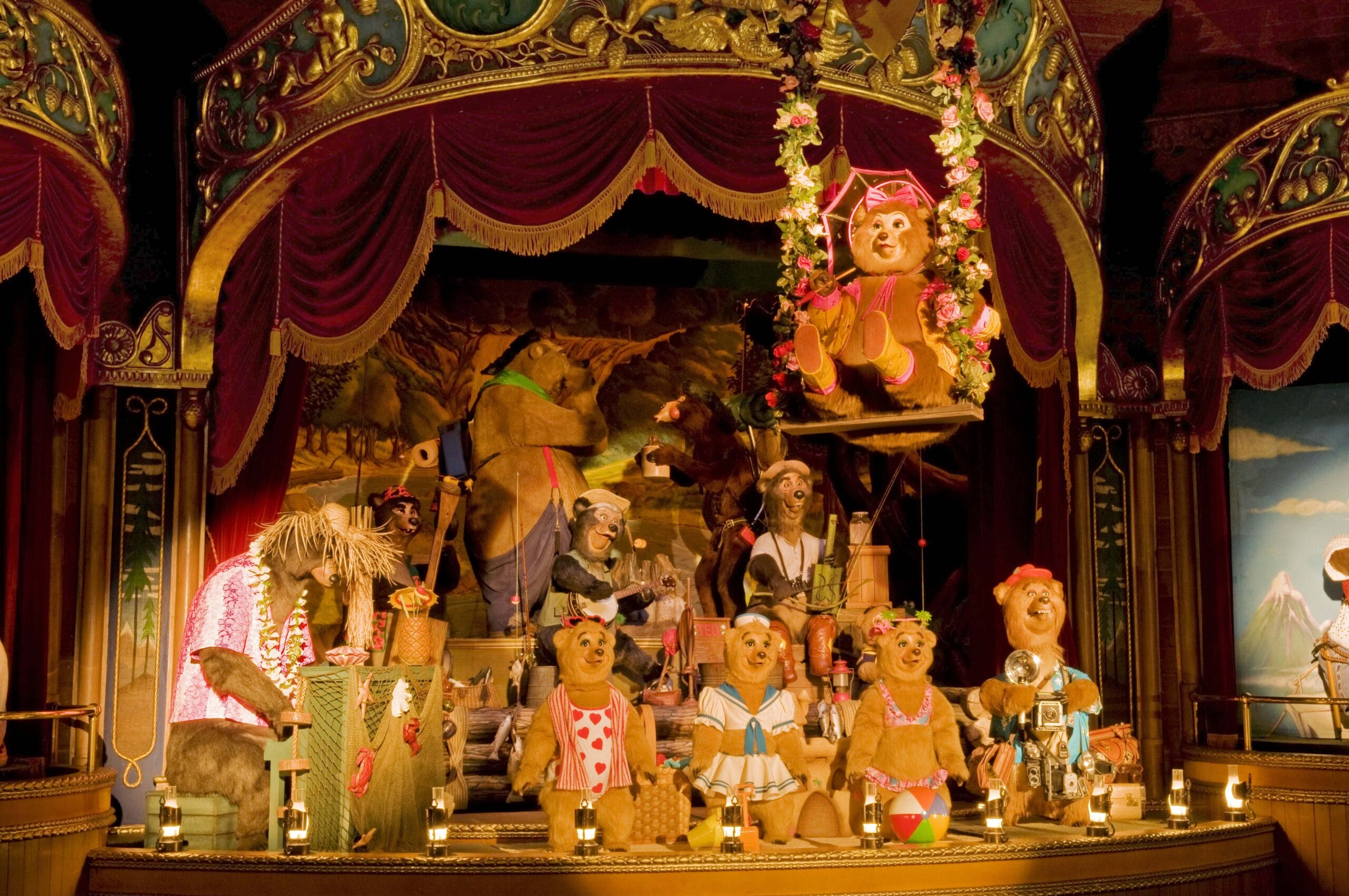 Animatronic bears perform on a decorated stage with red curtains and colorful costumes in a musical show setting.