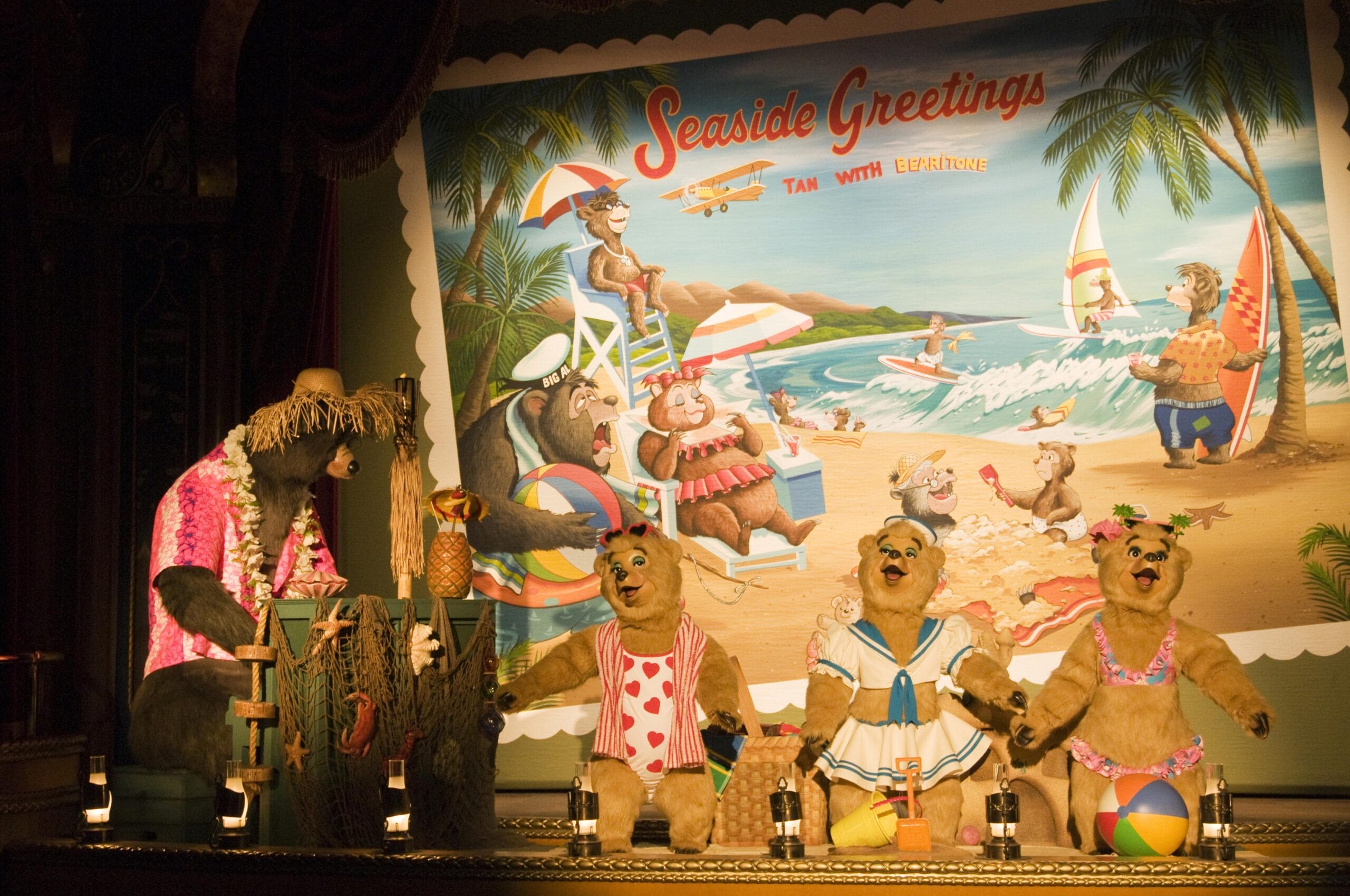 Four animatronic bears in beach outfits perform on stage with a “Seaside Greetings” tropical postcard backdrop.