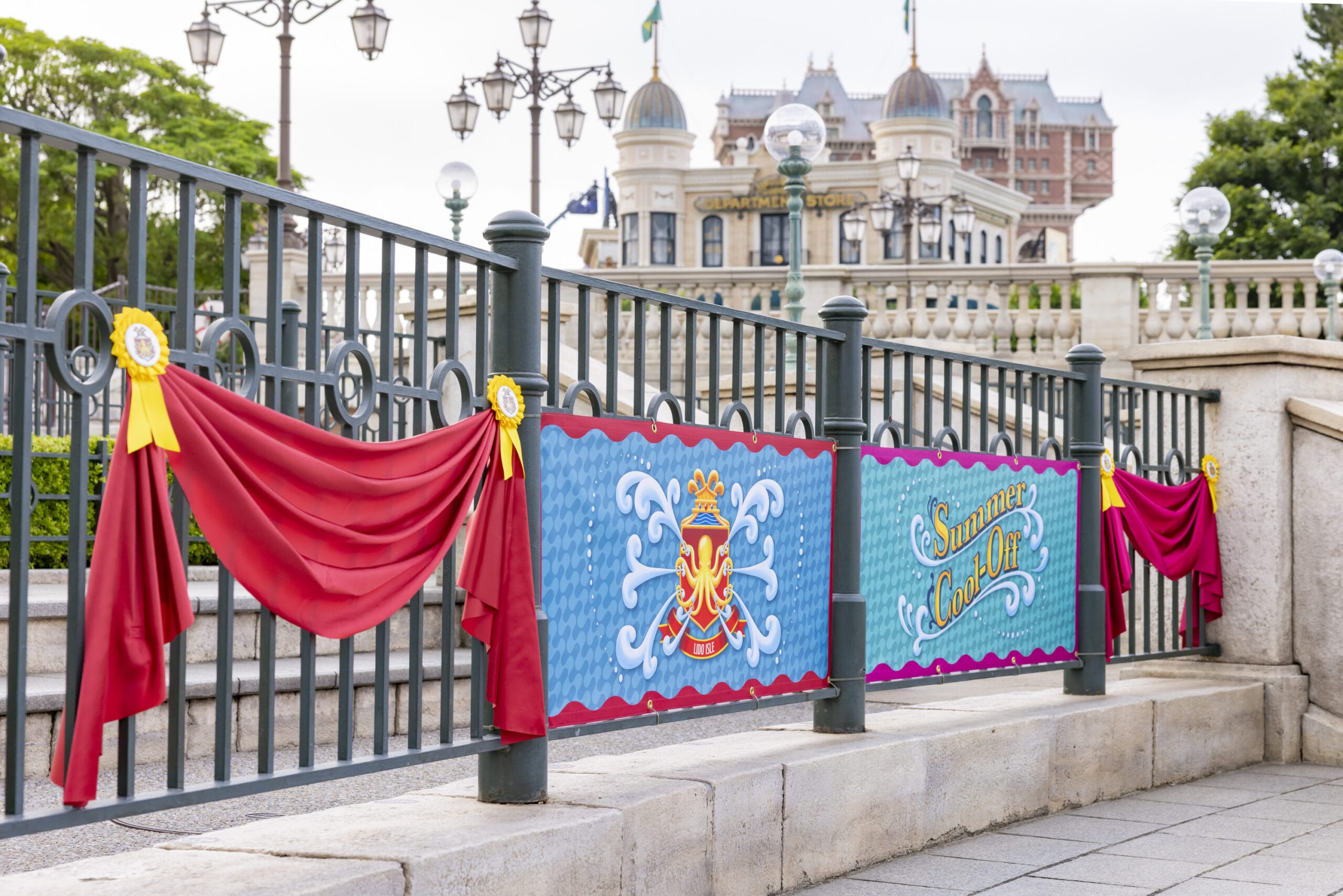 A festive "Summer Color Days" banner and red drapes decorate a black fence near steps and a grand building.