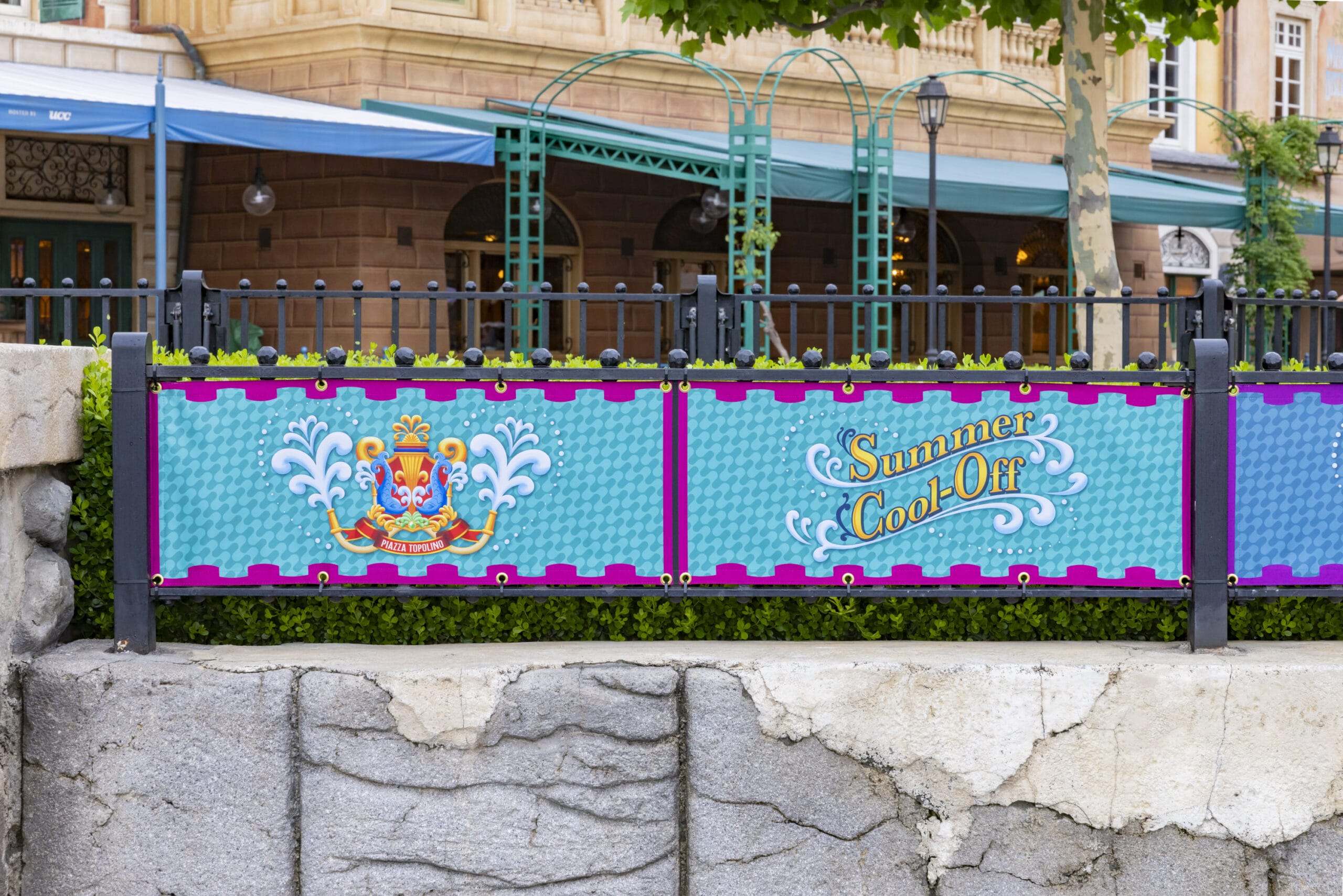 A colorful sign on a fence reads "Summer Cool-Off" with decorative designs and a crest on a blue background.