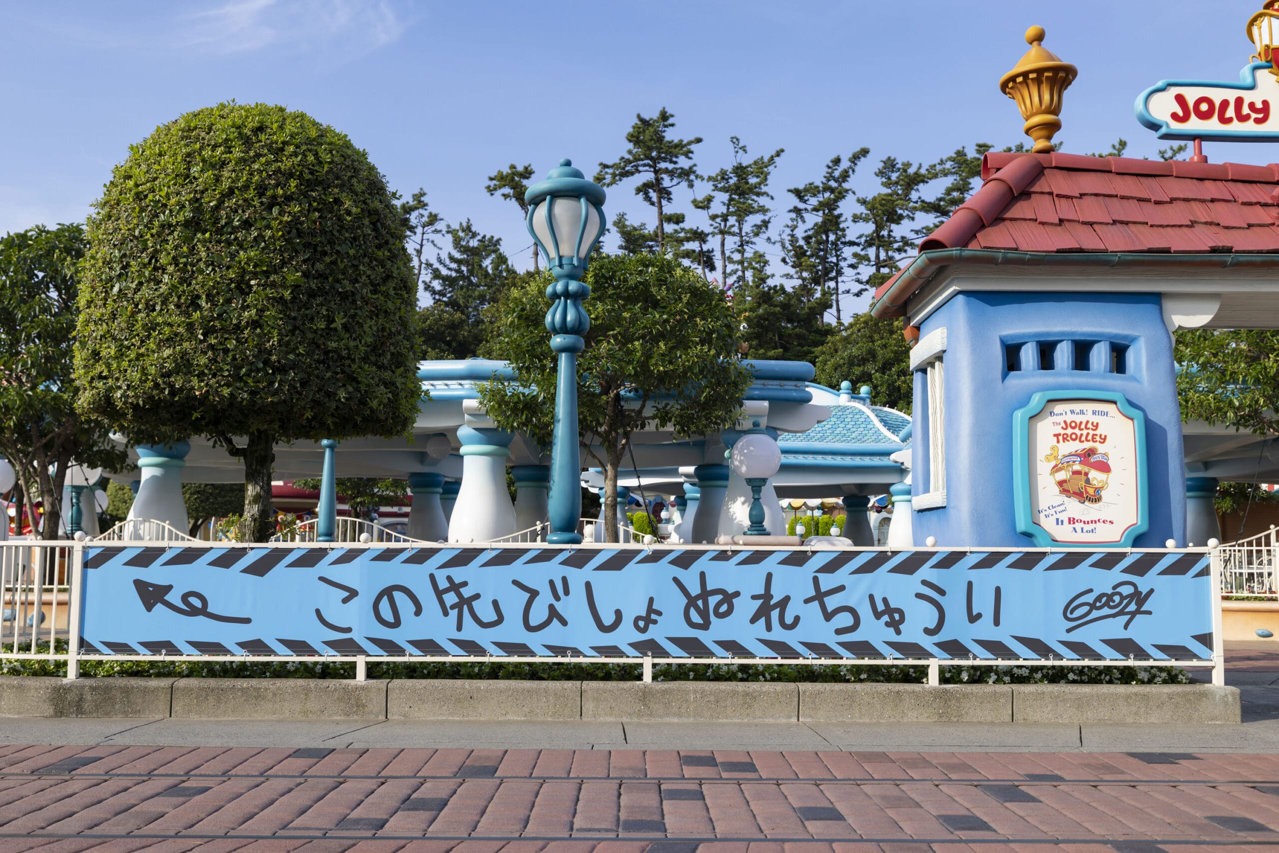 A blue fence with Japanese text and cartoon decorations in a whimsical outdoor theme park setting.