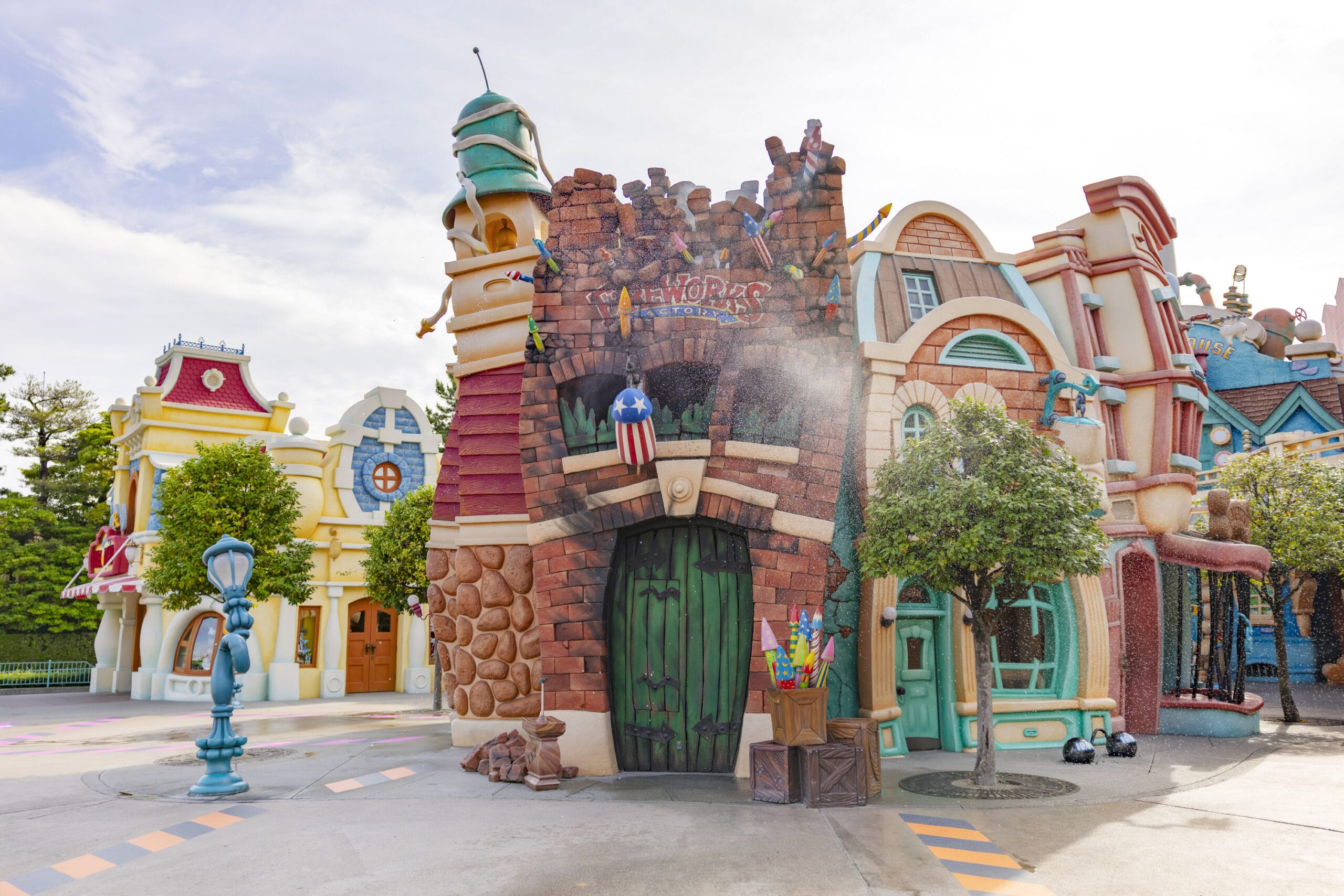 Colorful, cartoon-style buildings in a whimsical theme park, with trees and a lamppost nearby under a bright sky.