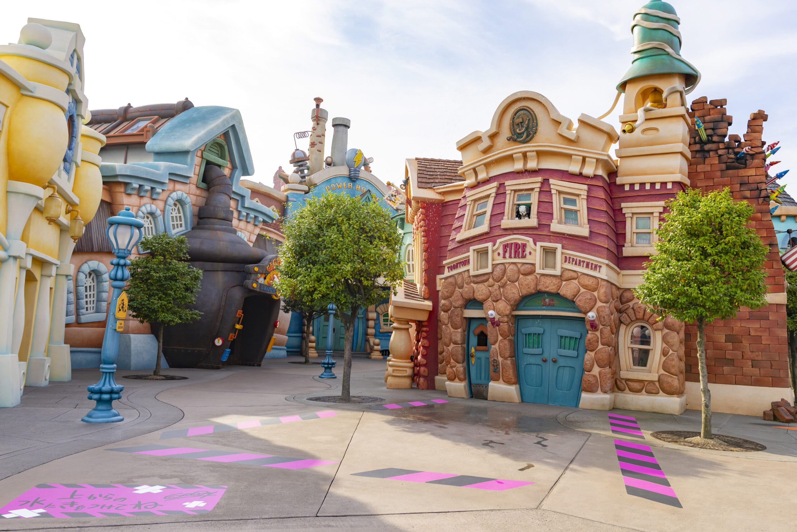 A colorful, cartoon-style street with whimsical buildings, trees, and pink-striped markings on the pavement.