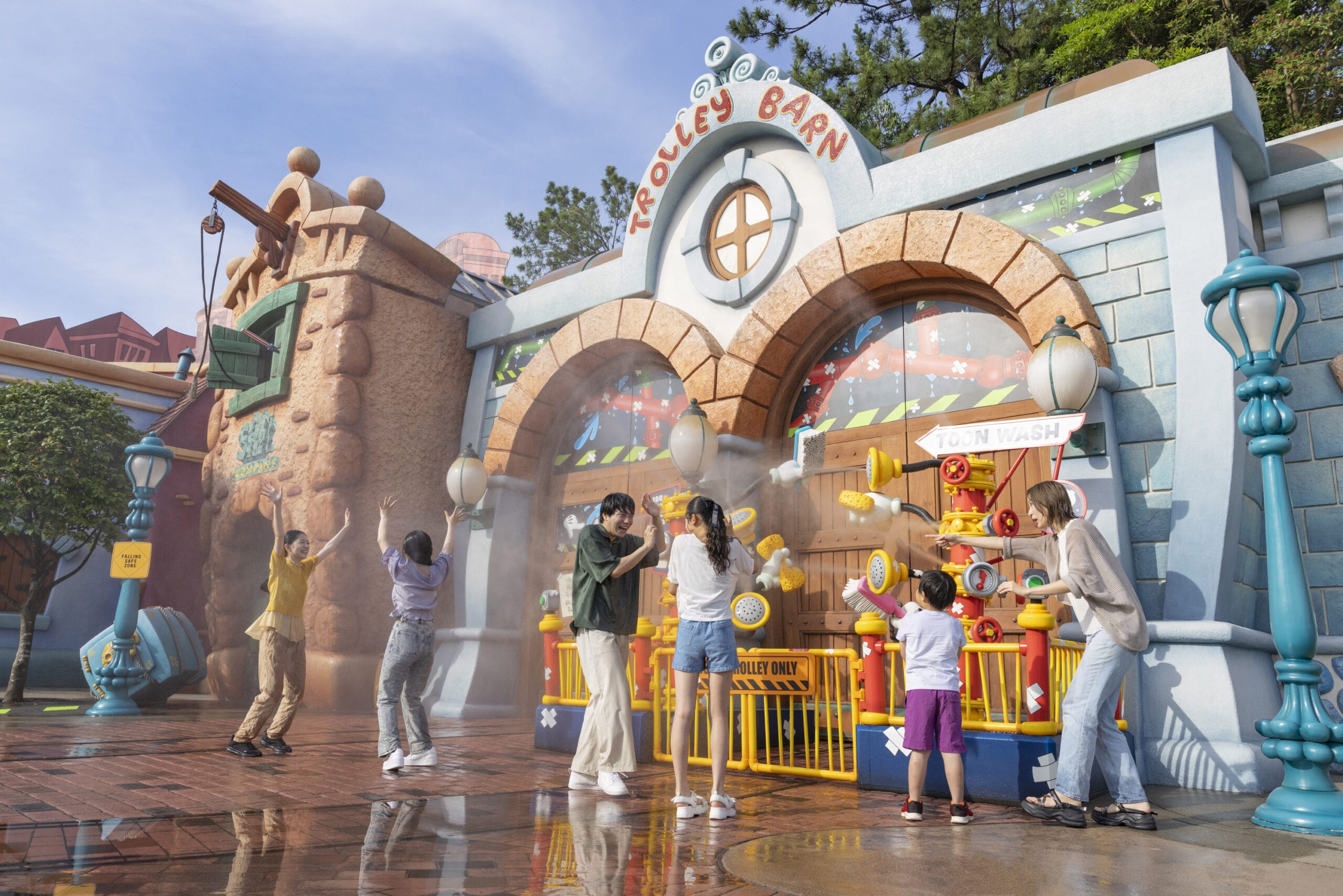 People play with water features outside a colorful Trolley Barn building at an amusement park on a sunny day.