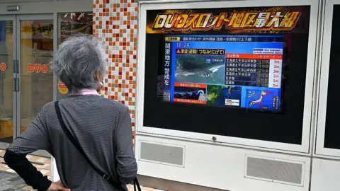 Getty Images A woman watches a television broadcast of a tsunami warning for much of coastal Japan following a 8.7 magnitude quake in the sea off eastern Russia