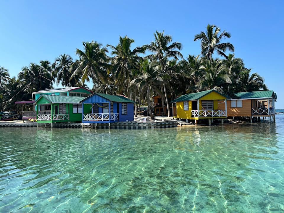 Colorful huts on stilts over clear water, surrounded by palm trees in a tropical setting. Ideal for a serene vacation escape