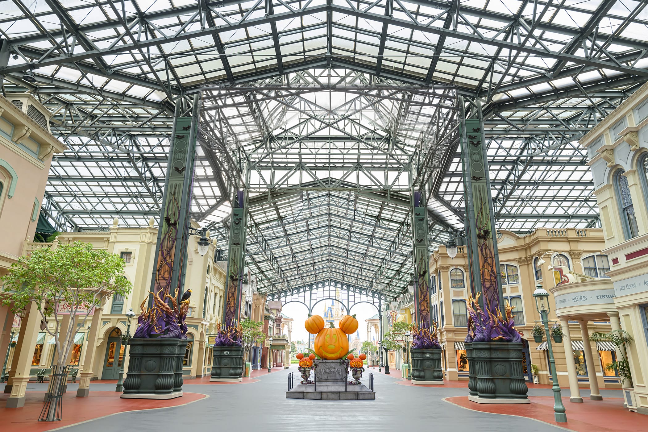 Spacious indoor street with glass roof at Tokyo Disney, Halloween pumpkin Mickey display, and decorated buildings on both sides.