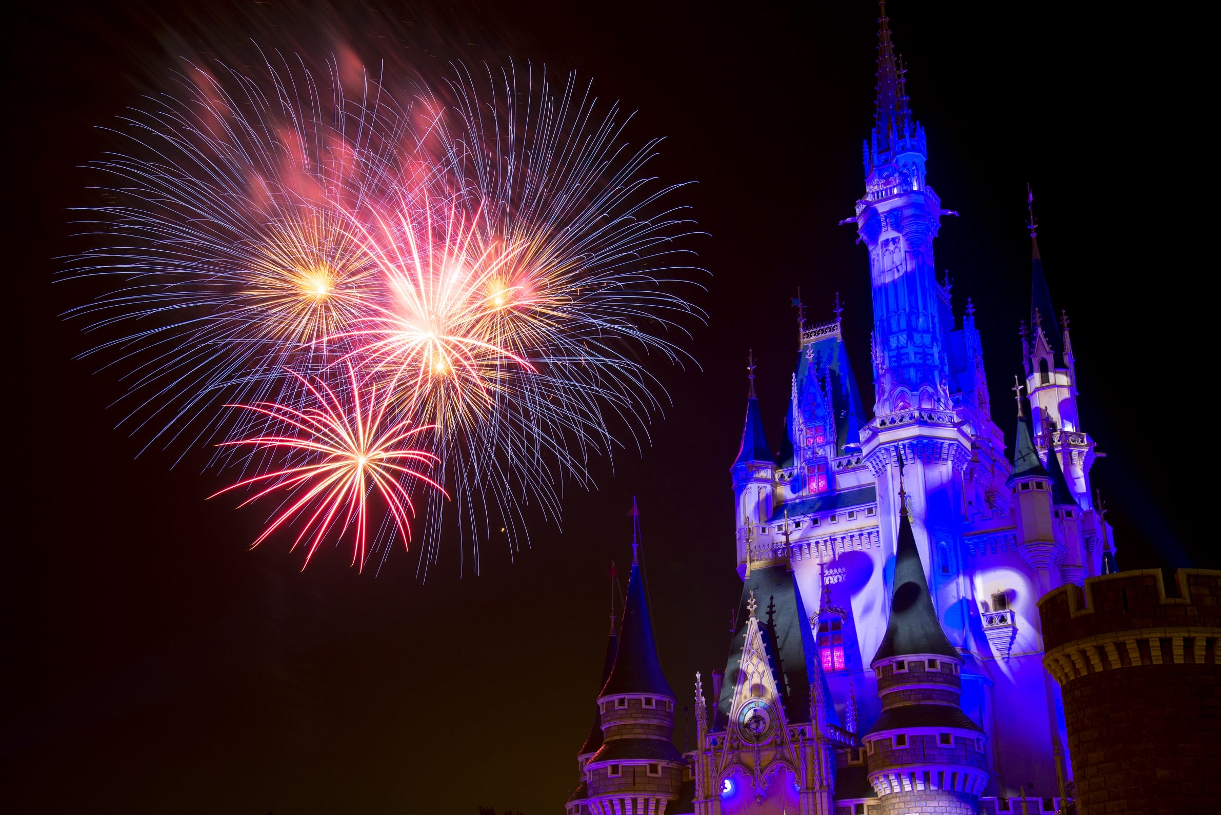 Colorful fireworks burst above Tokyo Disney Resort's fairy-tale castle, aglow with blue and purple Halloween lights.