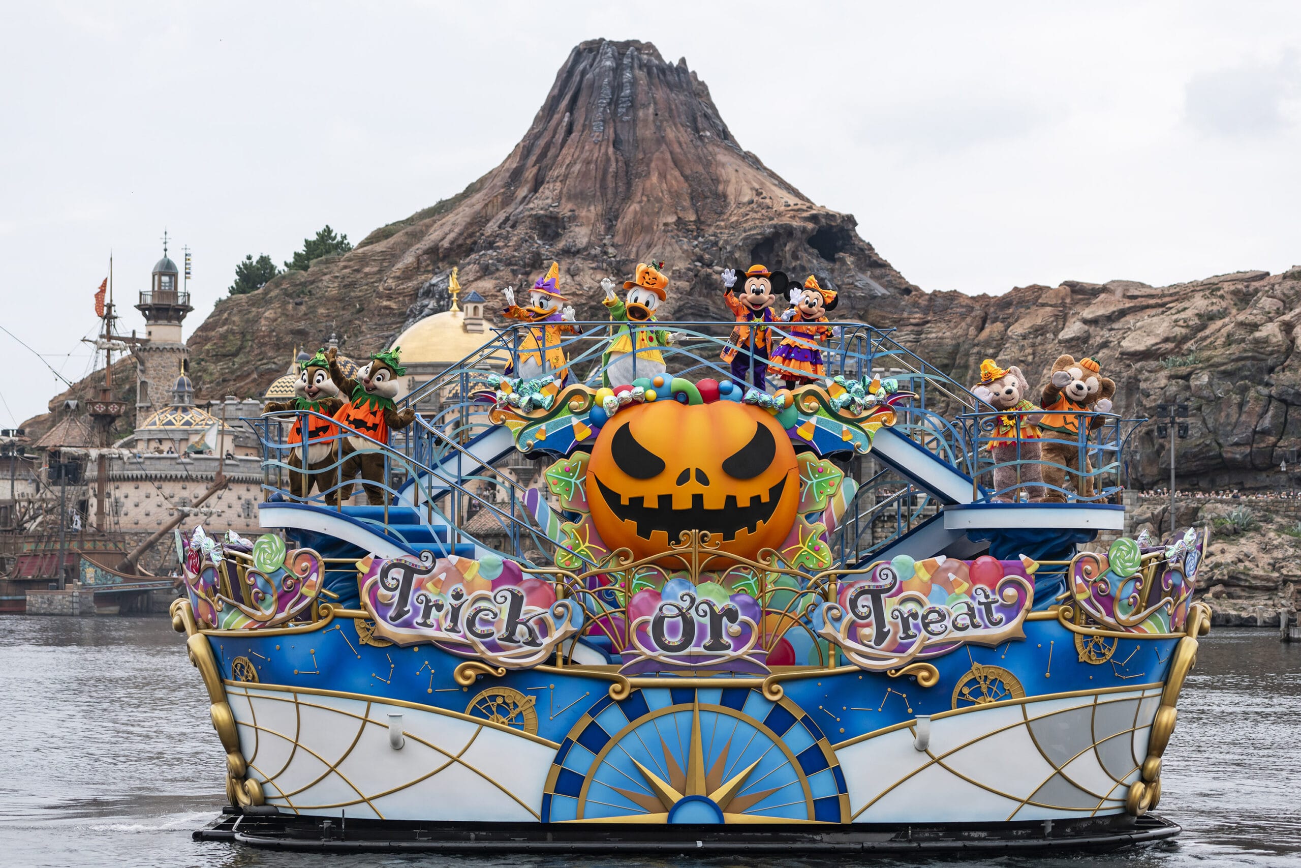 A festive Halloween 2025 parade float with Disney characters on water at Tokyo Disney Resort, pumpkin, and rocky mountain backdrop.